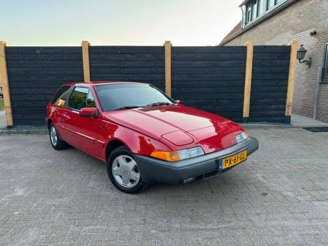 Röd Volvo 480 Turbo parkerad framför ett mörkt plank