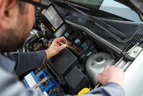 Person testar säkringar och reläer i en bils motorrum